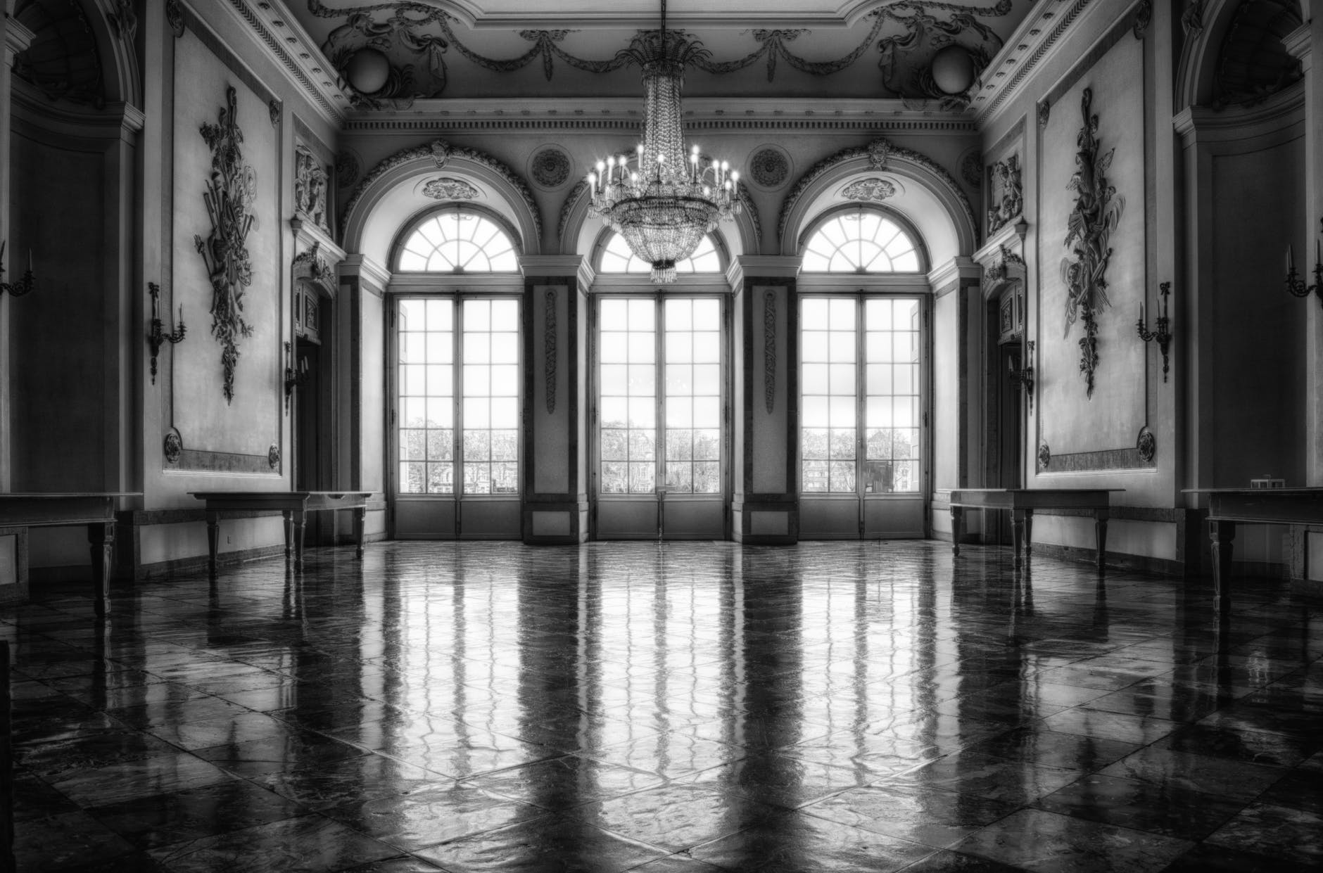 mansion great hall with Palladian doors and windows, crystal chandelier, floral carvings as decor on walls.