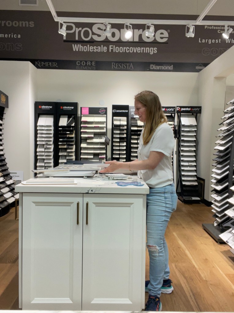 Woman, Tiffany, standing at counter island selecting quartz and tile materials for a project with samples of quartz on racks in the background of the room