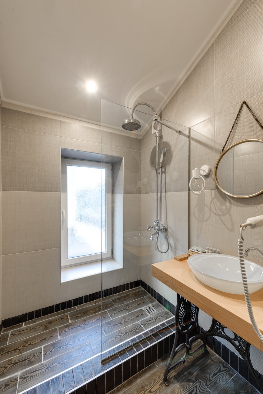 modern shower with glass panel, grey large tile walls, and dark grey wood tile flooring with bright overhead ceiling recessed can light