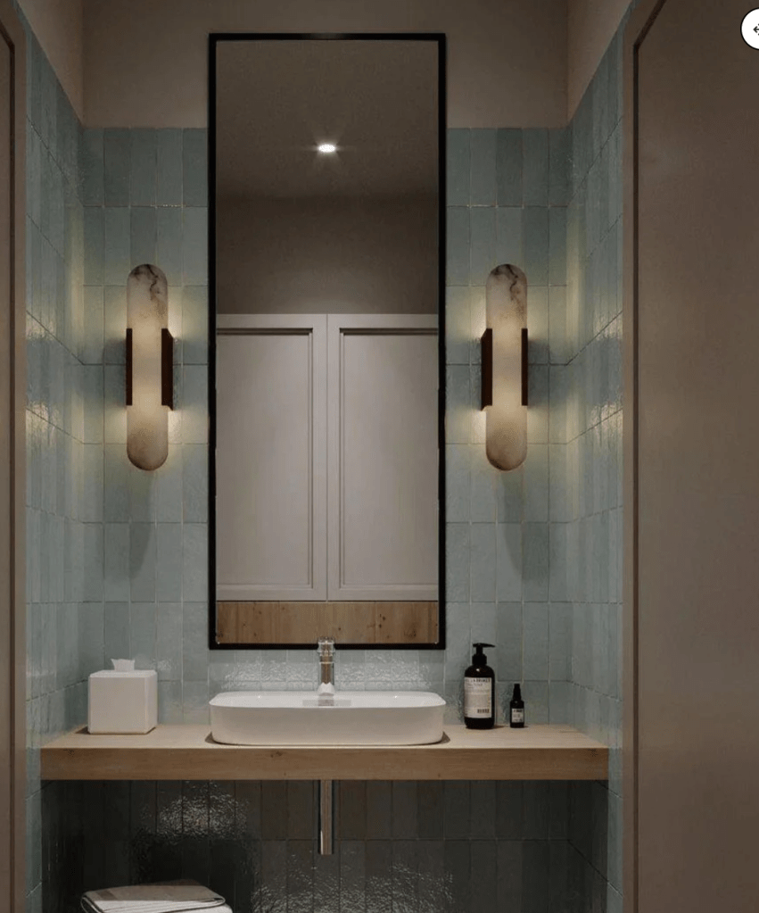 pair of shell sconces on left and right side of a very tall black framed rectangle mirror. with aqua ceramic tile on the wall above a white modern sink on top of a natural light wood counter 