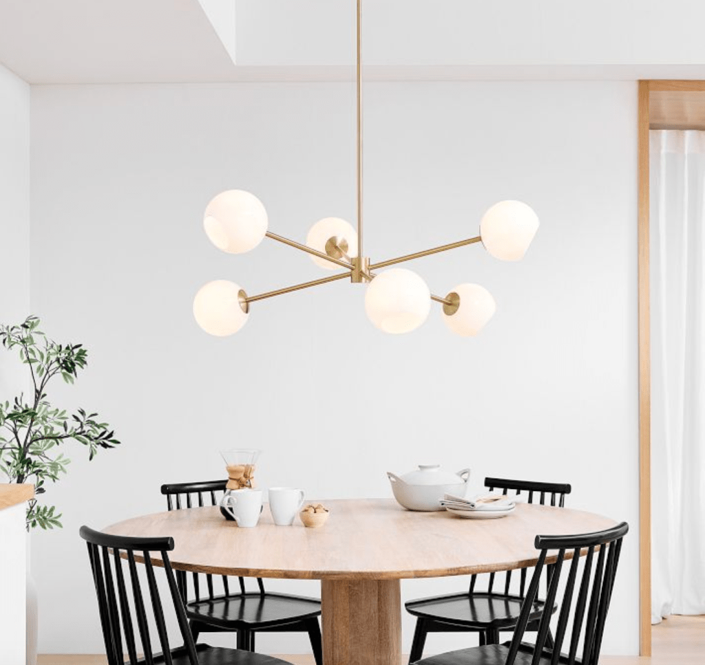West Elm Staggered Glass 6-Light Chandelier in Sputnik formation above natural wood round dining table with 4 black modern fam wooden chais with a white tea set on table