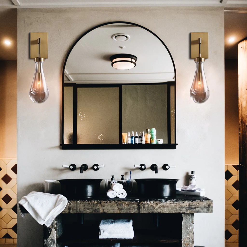 Denise Lamp Raindrop Wall Sconces on either side of a black framed arch mirror. 2 black sinks with a rustic raw wood open shelf vanity