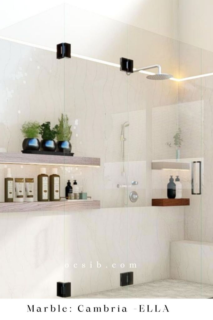 3D rendering of a shower with white marble with glass panel doors, nickel rain shower faucet, and wood floating shelves with plants and shampoo bottles on them white text reads ocsib.com marble: cambria ella