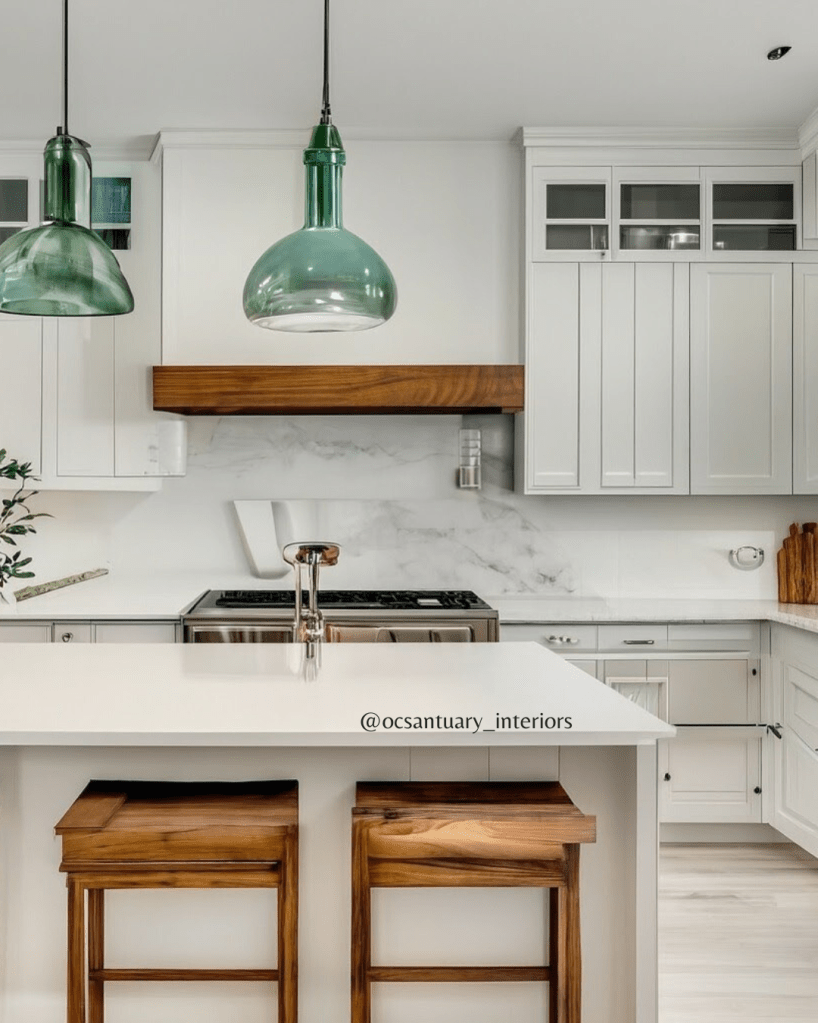 white kitchen with white shaker kitchen cabinets, wooden counter stools, white quartz countertop, stainless steel sove with wood trim white hood and aqua glass pendants over kitchen island.